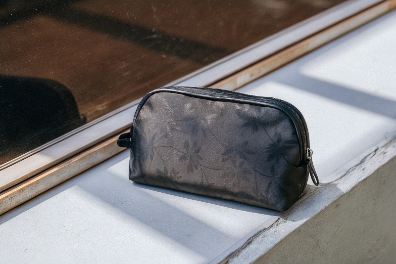 A dark, matte black cosmetic box where a subtle floral pattern is revealed by the reflection of light on the Spot UV finish.