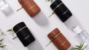 Bamboo leather perfume travel cases in black and brown, displayed with fragrance bottles and greenery on a textured white background.