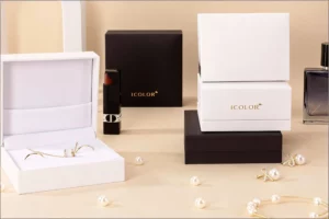 A set of luxury white and brown rigid jewelry gift boxes with the ICOLOR logo, arranged with gold rings, a necklace, pearls, lipstick, and perfume on a beige background. Elegant high-end product display for branding and packaging design.