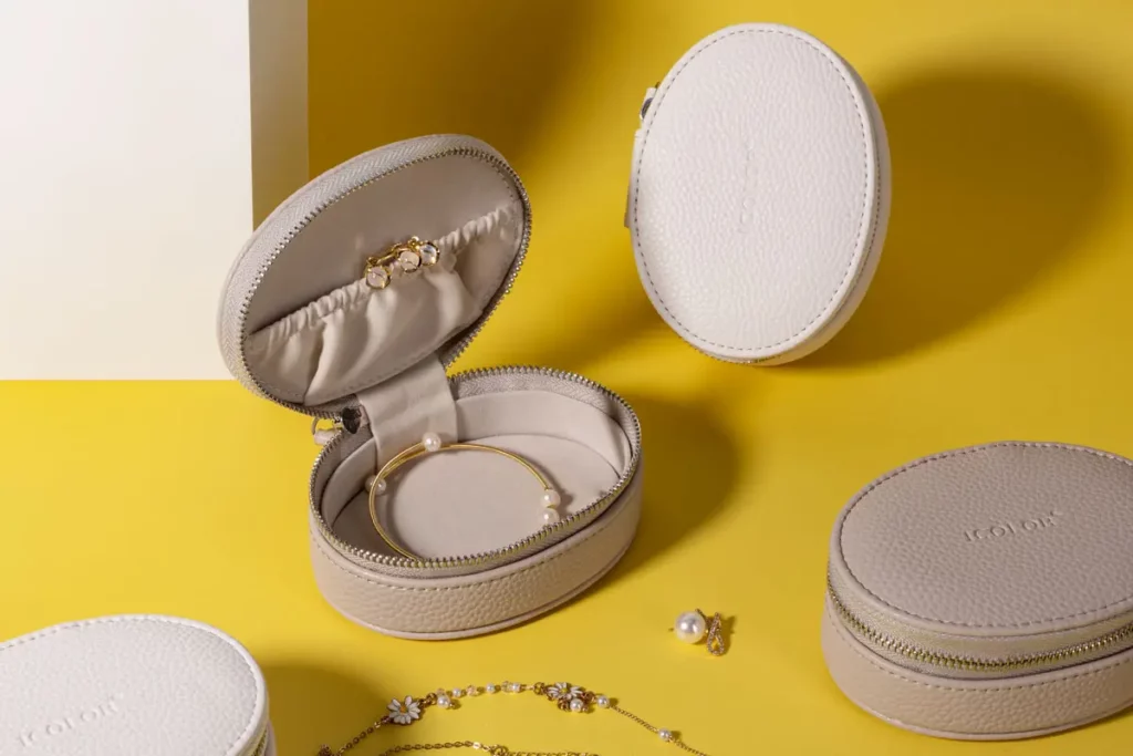 Round recycled leather jewelry cases in beige, displayed with earrings, bracelets, and accessories on a vibrant yellow background.